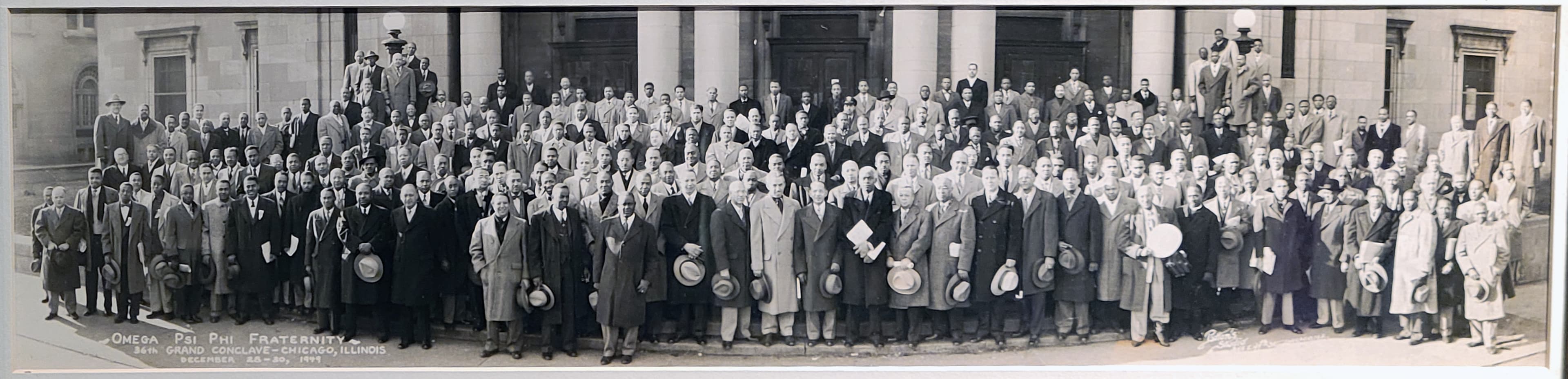 Official panoramic photograph of the 36th Grand Conclave: roughly two hundred and fifty Omega men in overcoats and hats arrayed in rows on the steps of a columned building, with the inscription 'Omega Psi Phi Fraternity, 36th Grand Conclave — Chicago, Illinois, December 28-30, 1949' lettered across the lower left